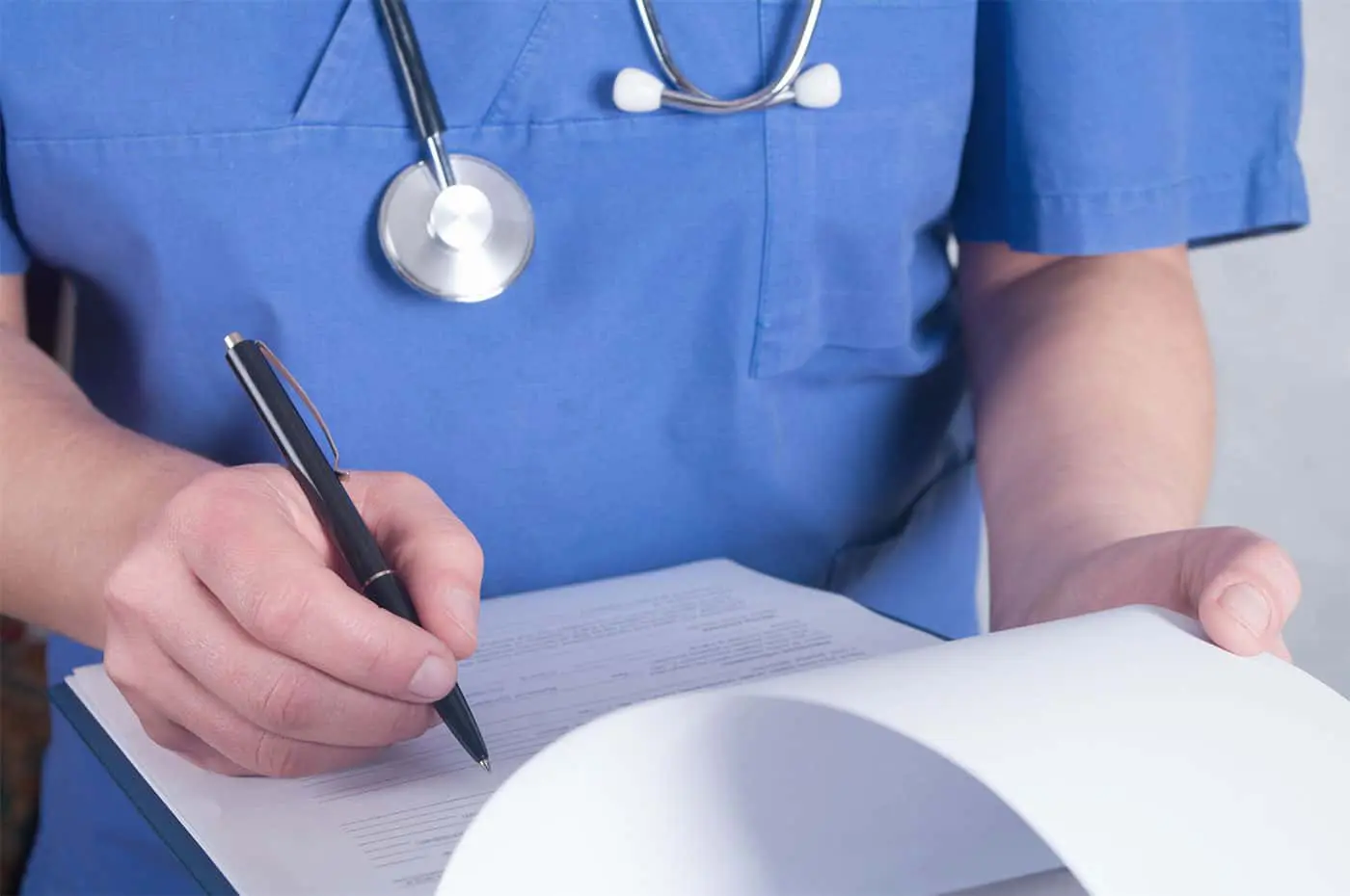 A doctor writing on paper with stethoscope around neck.