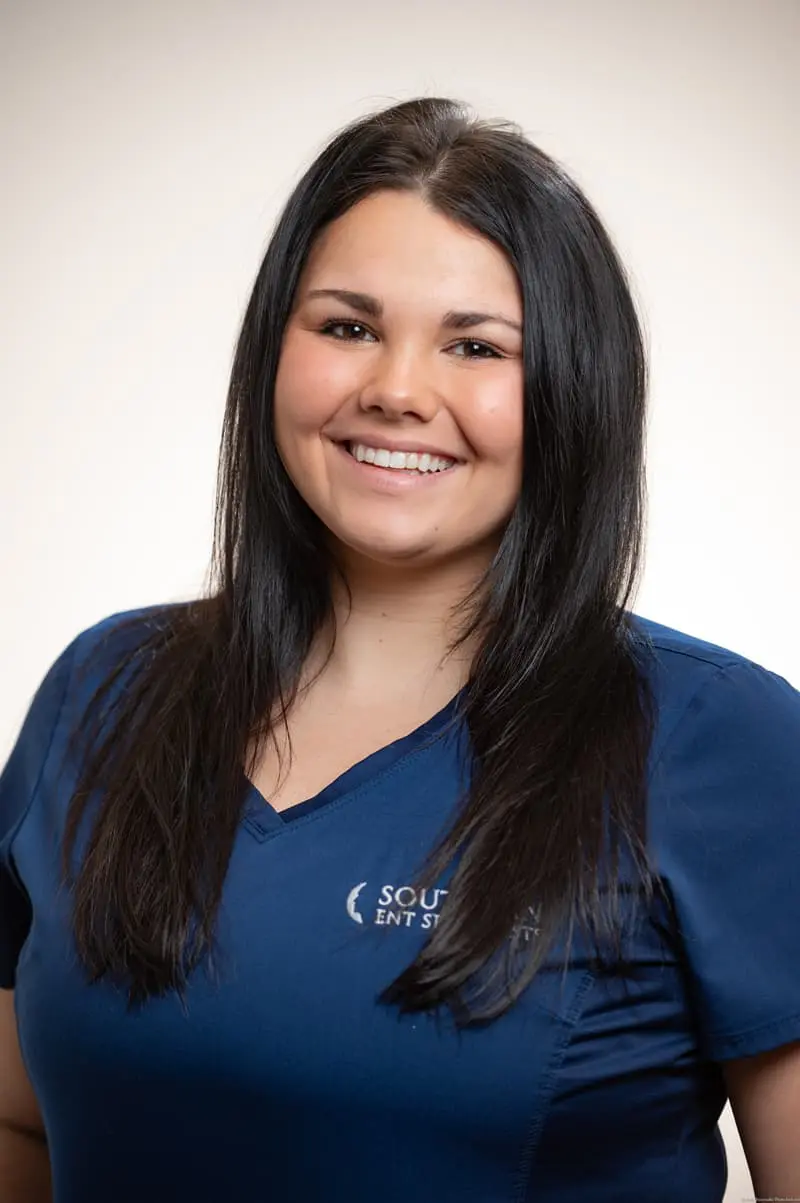 A woman in blue scrubs smiles for the camera.